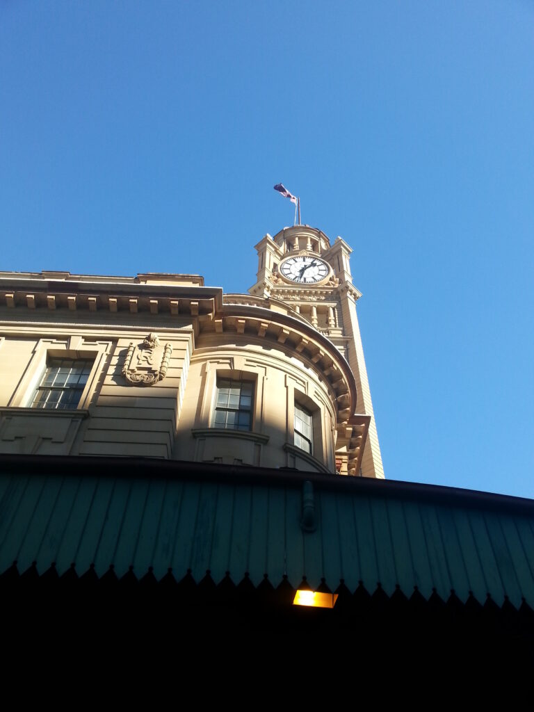 Clock tower of Sydney Central Station rising above the station awning against a clear blue sky.