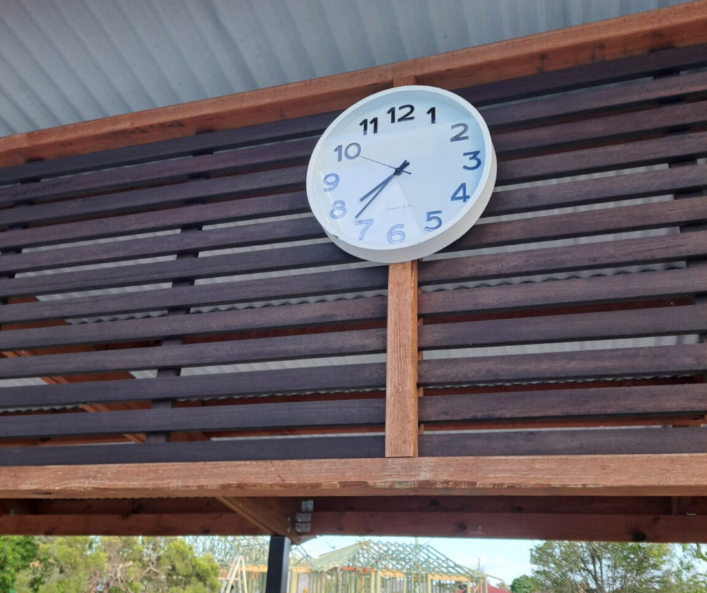 Outdoor pool clock mounted above a timber structure, returned after being repaired.